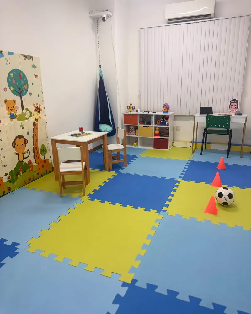 Sala de atendimento da Semear com piso emborrachado colorido, mesinha infantil, balanço casulo e estante de brinquedos